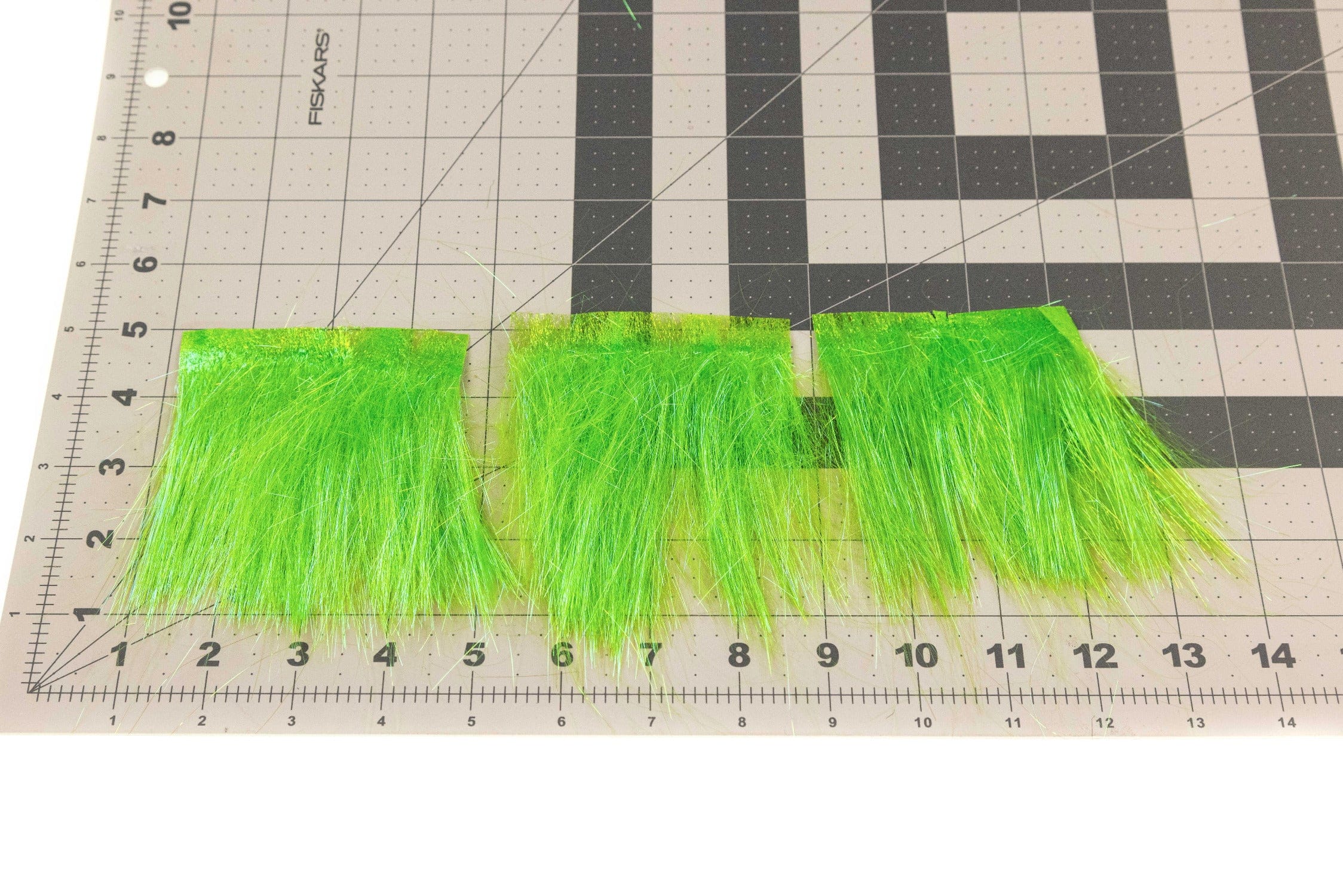 Neon chartreuse Hareline Ice Dub shimmer fringe, synthetic iridescent fly tying fibers in three taped strips on grid mat
