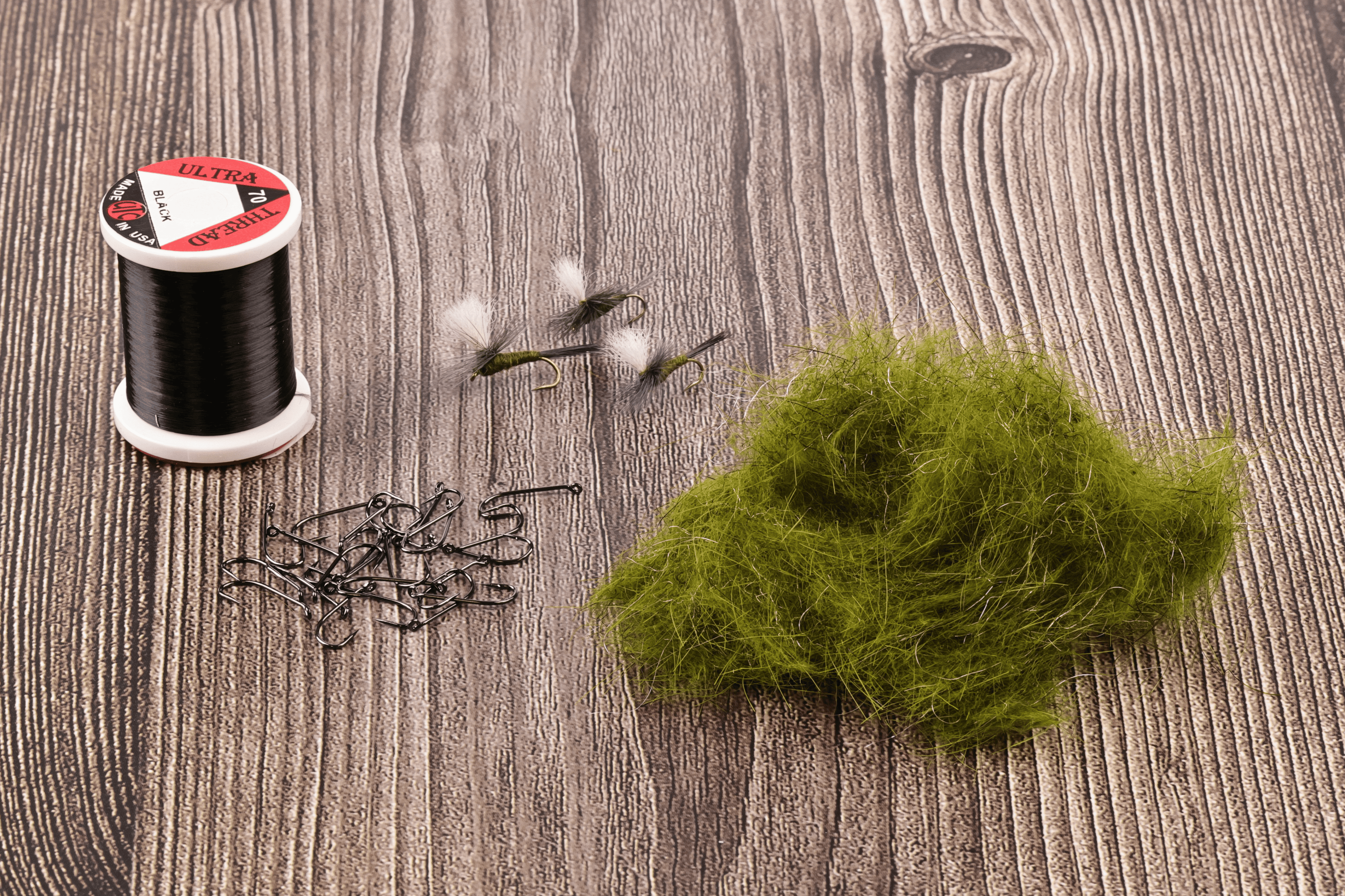Olive green Hareline Ice Dubbing clump with black thread spool, hooks and small parachute dry flies for fly tying