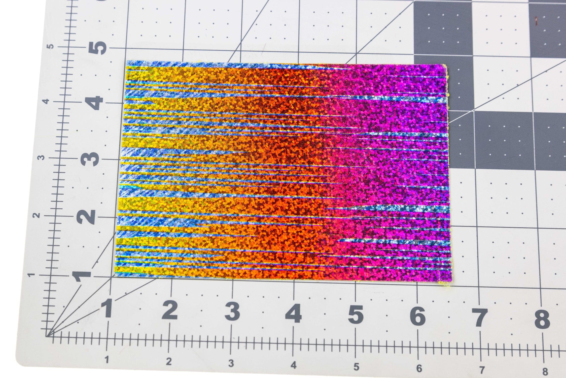 Hareline Lycra Foil Stretch holographic sheet in orange, pink, yellow and blue stripes on grid mat, fly tying material