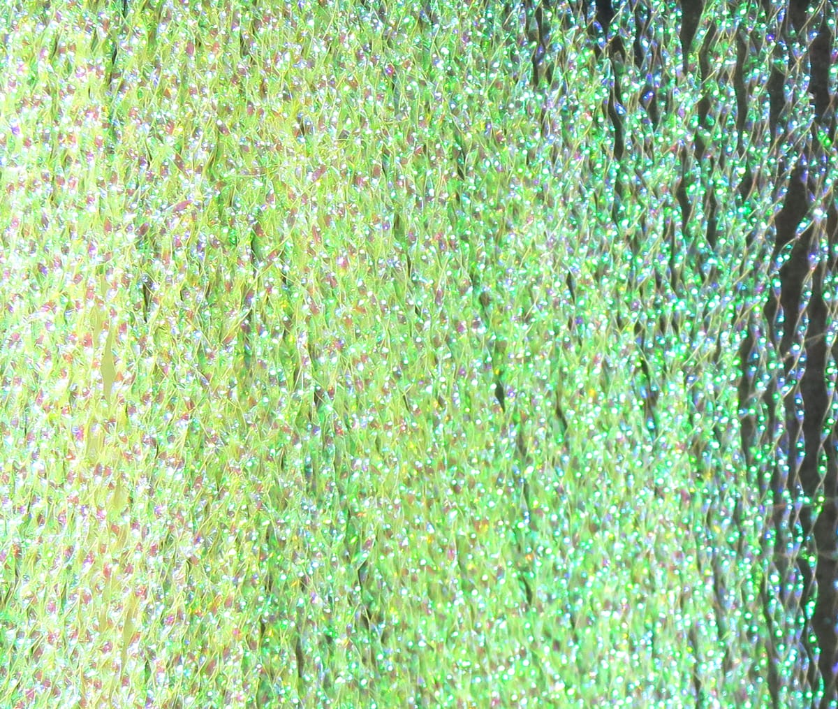 Iridescent chartreuse-green synthetic flash fibers with fine holographic strands, shimmering texture for fly tying