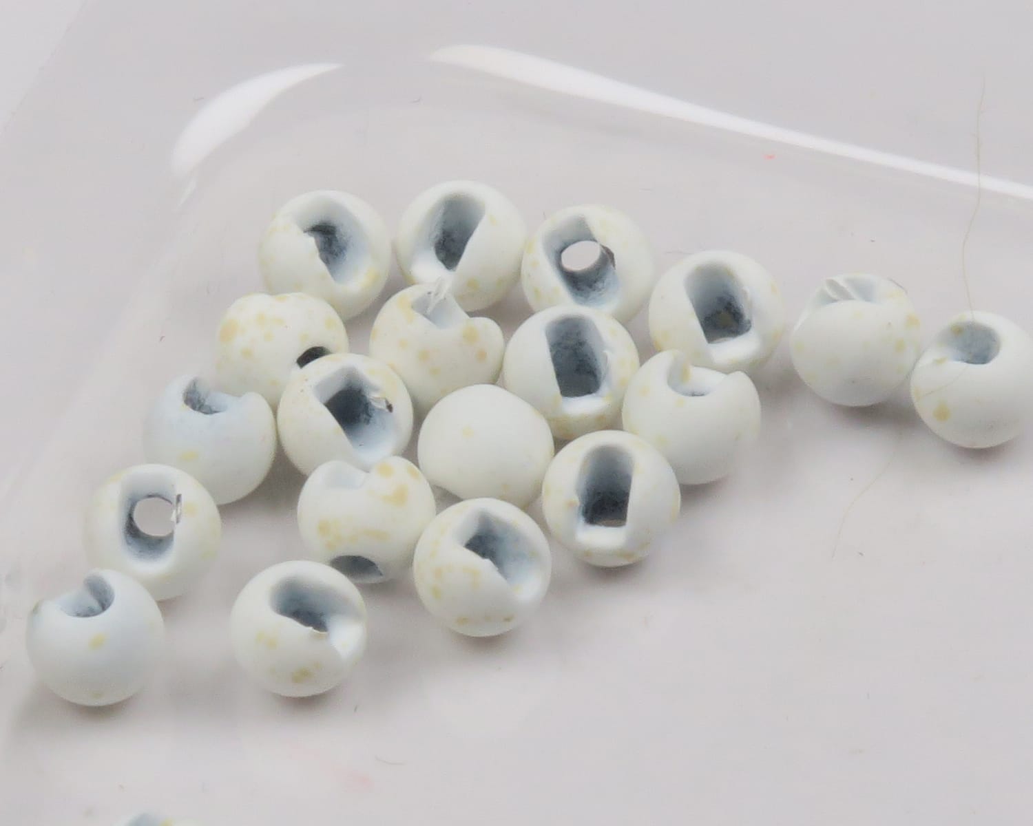 White mottled tactical slotted tungsten beads with pale yellow speckles and gray-blue slots for fly tying