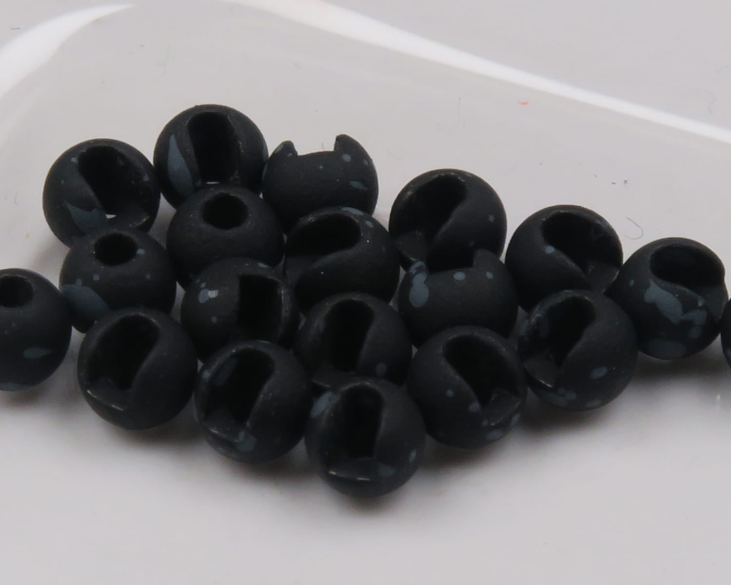 Matte black mottled slotted tungsten beads with gray speckles, round fly tying beads on white background