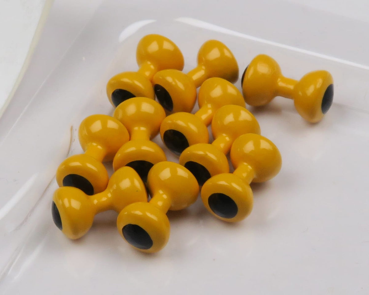 Glossy mustard-yellow painted lead eyes with matte black centers, double-ended fly tying eyes on white tray