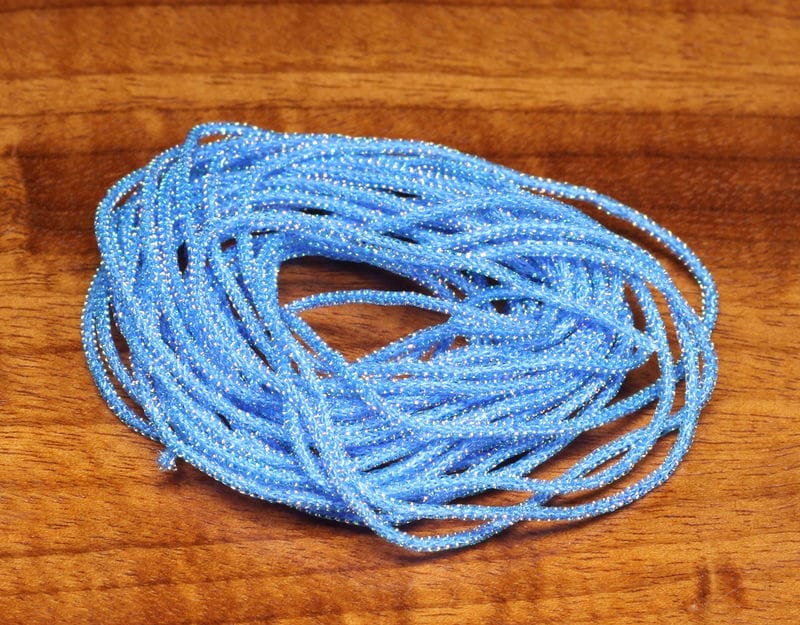 Hareline Pearl Core Braid bright blue pearlized braided cord for fly tying, coiled on a wooden surface