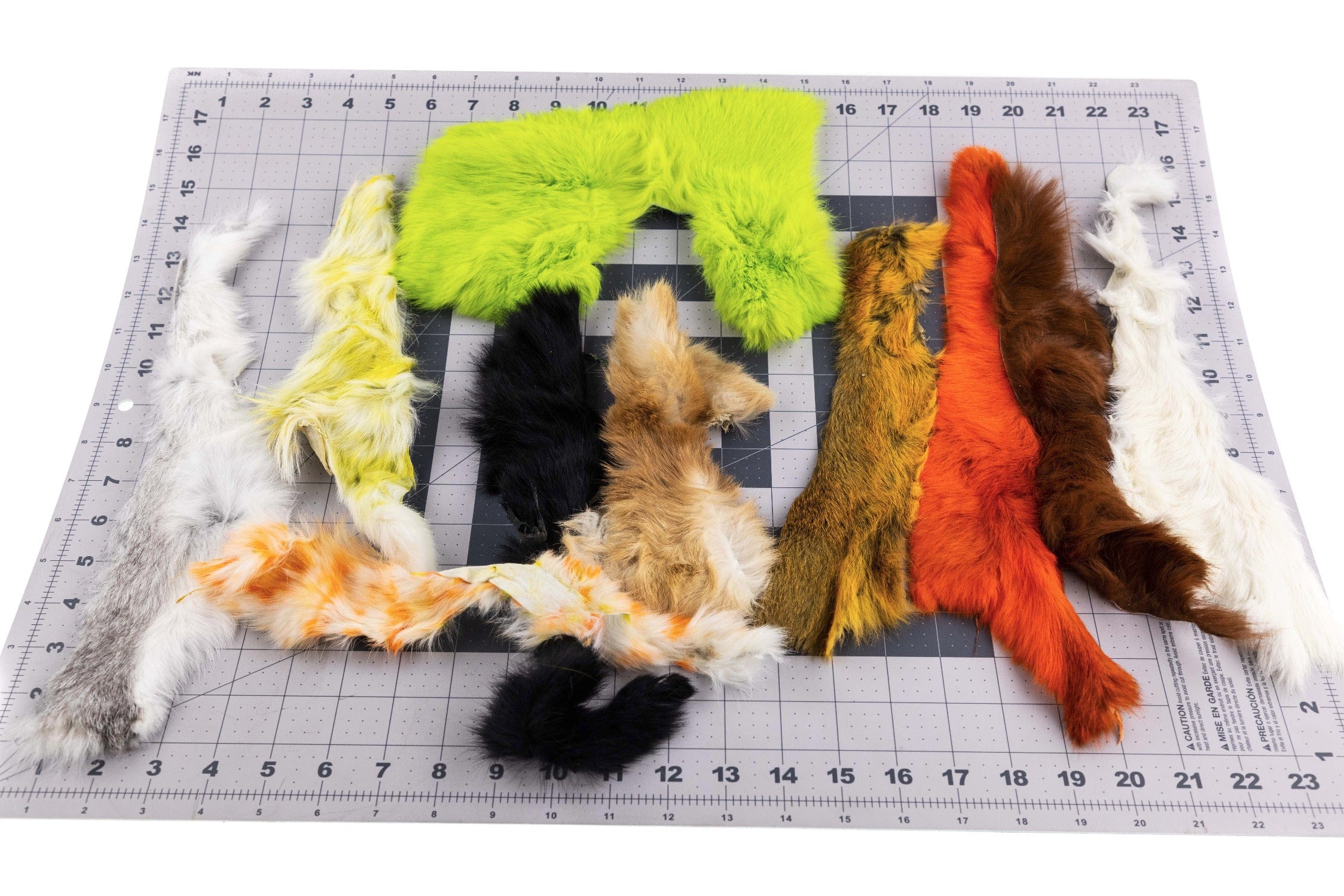 Assorted dyed rabbit hide strips in chartreuse, orange, brown, black and white laid on cutting grid for fly tying