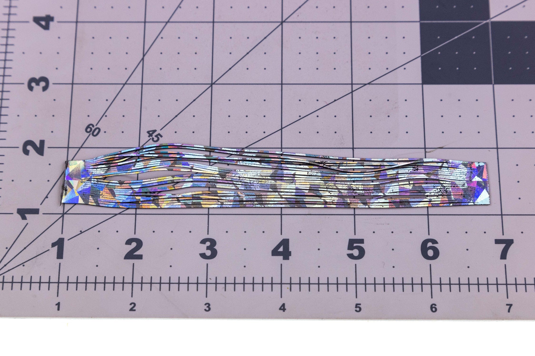 Iridescent rainbow shimmer legs for fly tying, thin holographic synthetic strips laid on gridded cutting mat with ruler