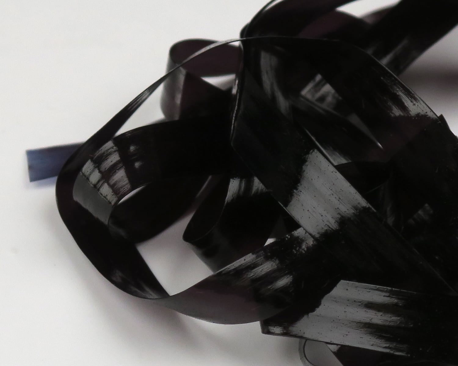 Black glossy synthetic Scud Back strips curled on white background for fly tying, reflective sheen.