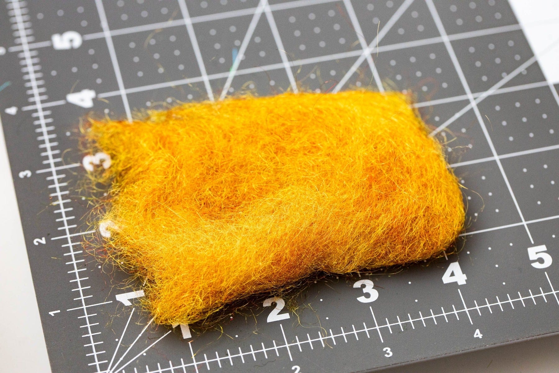 Bright golden-orange Hareline STS trilobal dubbing pad, fuzzy synthetic fibers for fly tying on cutting mat grid
