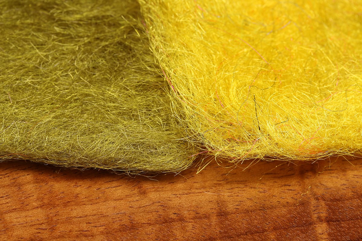 Two pads of Swiss Straw fly tying material in olive and bright yellow with fine shiny synthetic fibers on wooden surface