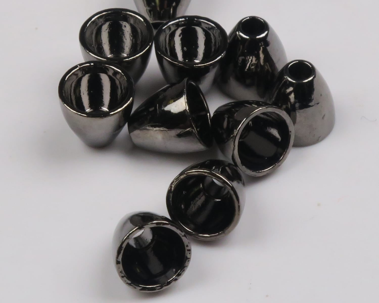 Glossy gunmetal tungsten cones scattered on white, small conical fly tying beads with smooth reflective finish