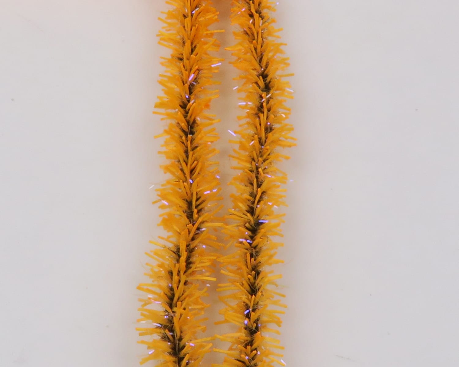 Two bright orange UV Badger Flexi Squishenille chenille strands with dense fuzzy bristles and purple flash for fly tying