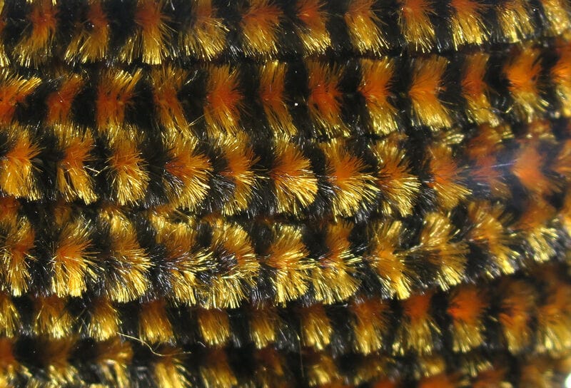 Hareline gold and orange variegated chenille with black accents, metallic fuzzy fibers for fly tying