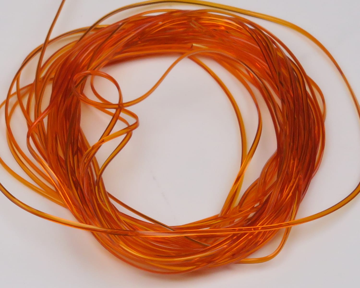 Coiled translucent orange vinyl rib strands, glossy thin flexible tubing used for fly tying accents