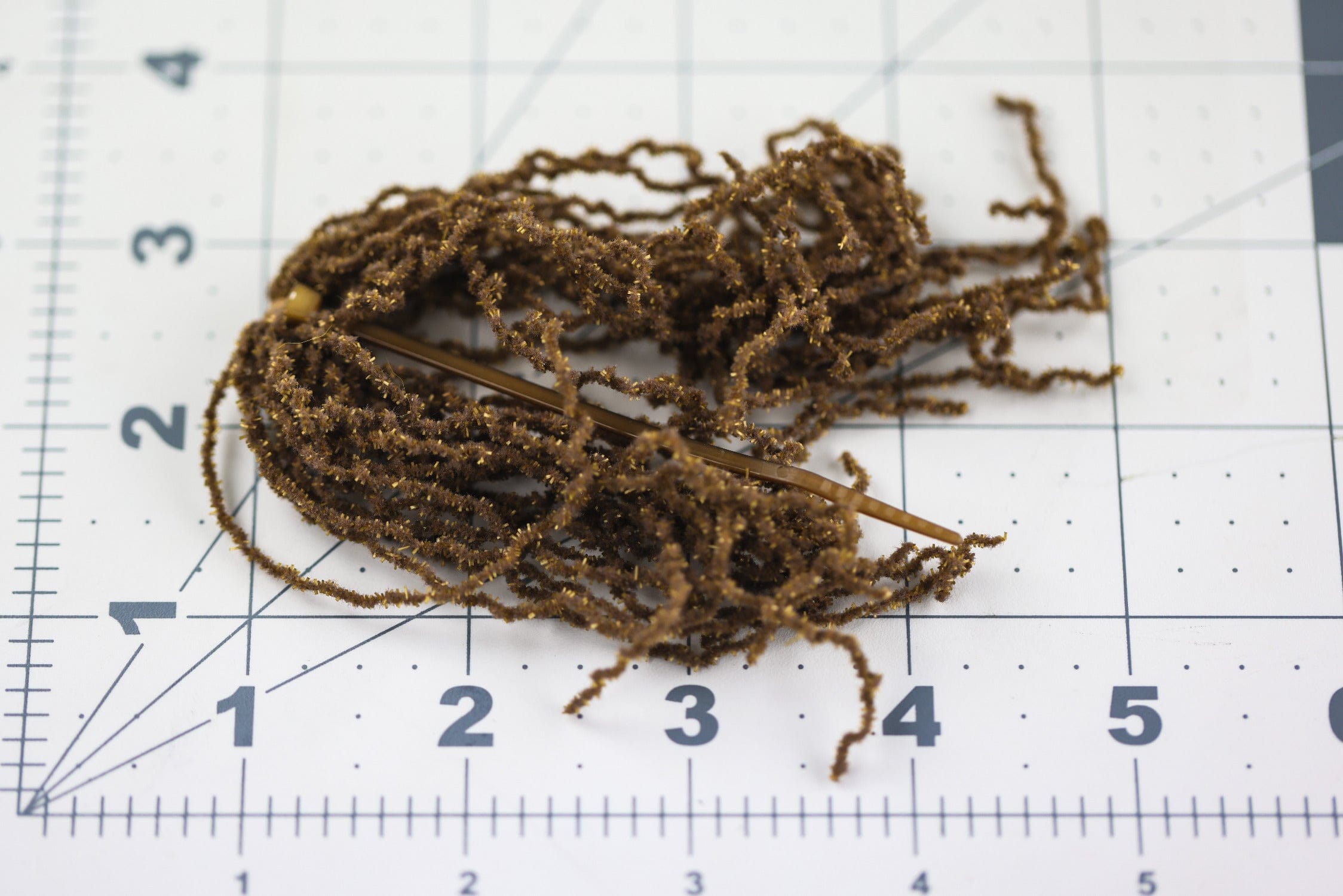 Brown Hareline Wormille curly chenille with gold flash, textured synthetic strands for fly tying, shown on grid mat