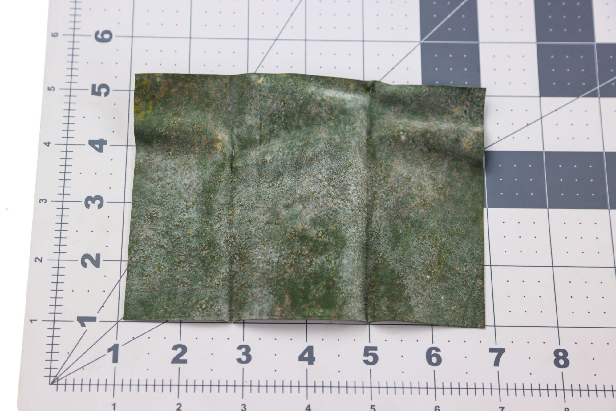Kiley's Exo Skin green mottled textured sheet with rust-gold specks on cutting mat, fly tying material
