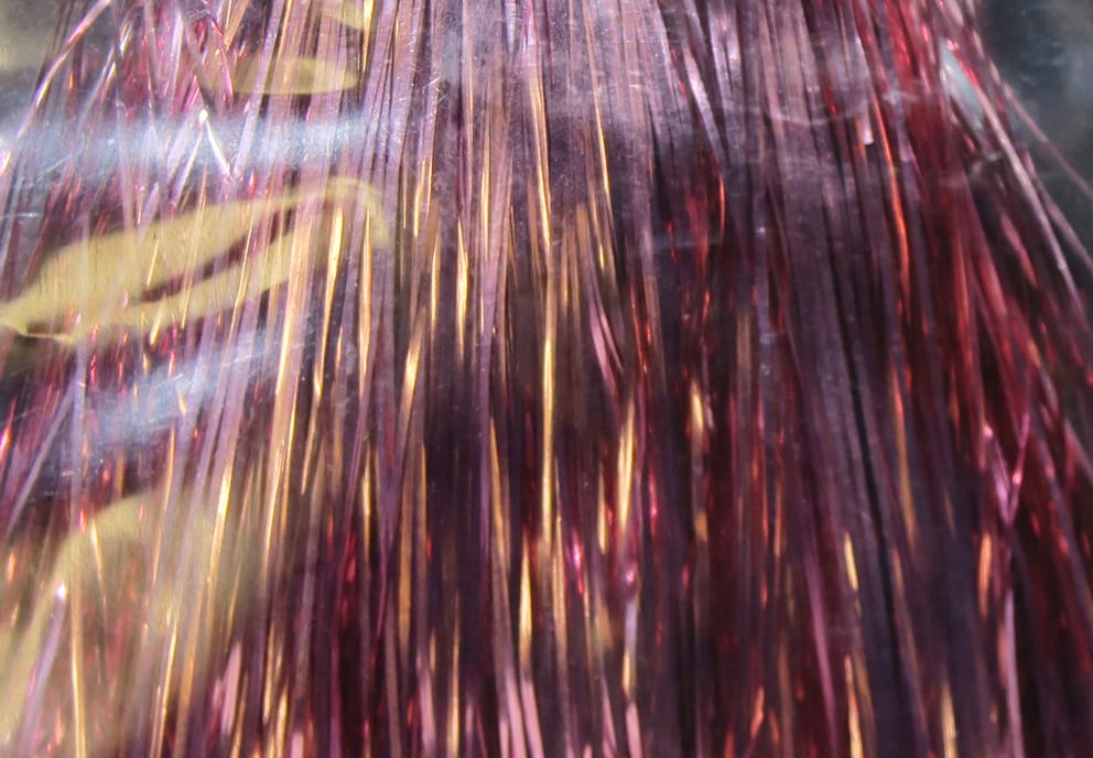Shimmering Hedron Flashabou metallic tinsel strands in pink-purple with copper highlights, thin iridescent fly tying material