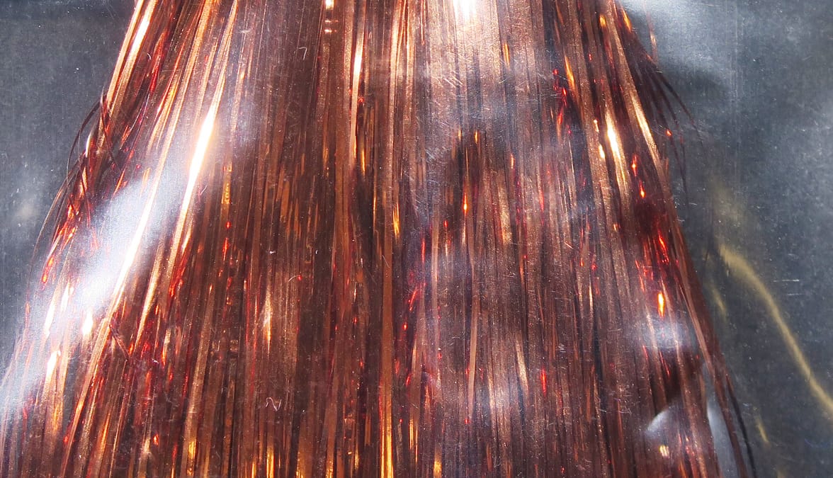 Copper-bronze Hedron Flashabou strands, thin metallic tinsel fibers with red shimmer, reflective fly-tying material