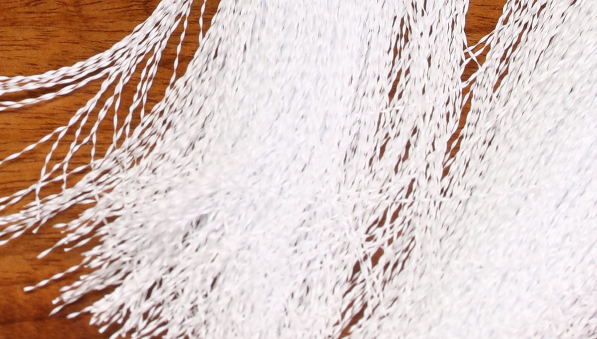 White Hedron Flashabou Accent twisted synthetic strands for fly tying, fine shimmering fibers on wood background