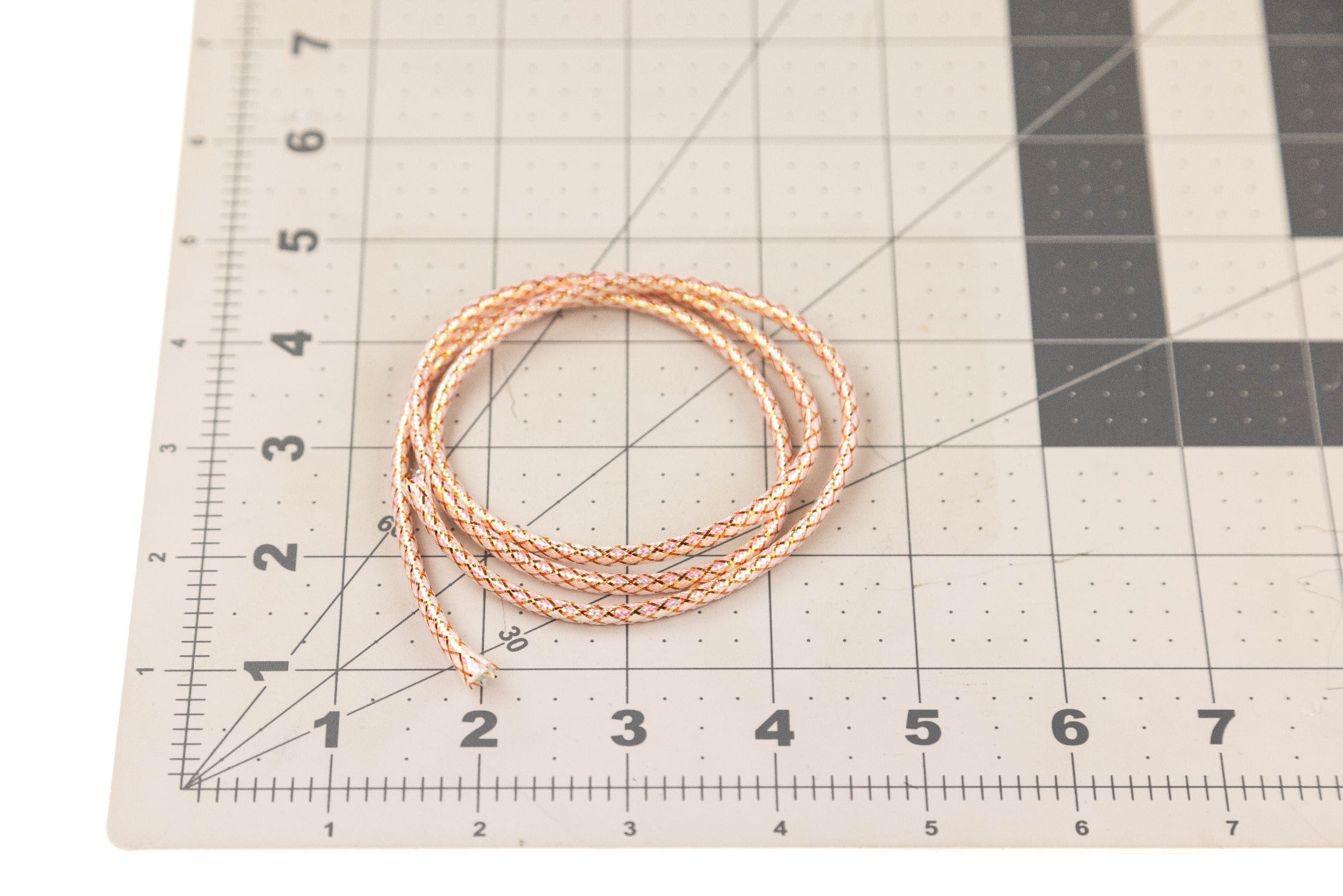 Coiled Hedron Flashabou minnow body tubing in peach, gold and white braided reflective material on grid cutting mat