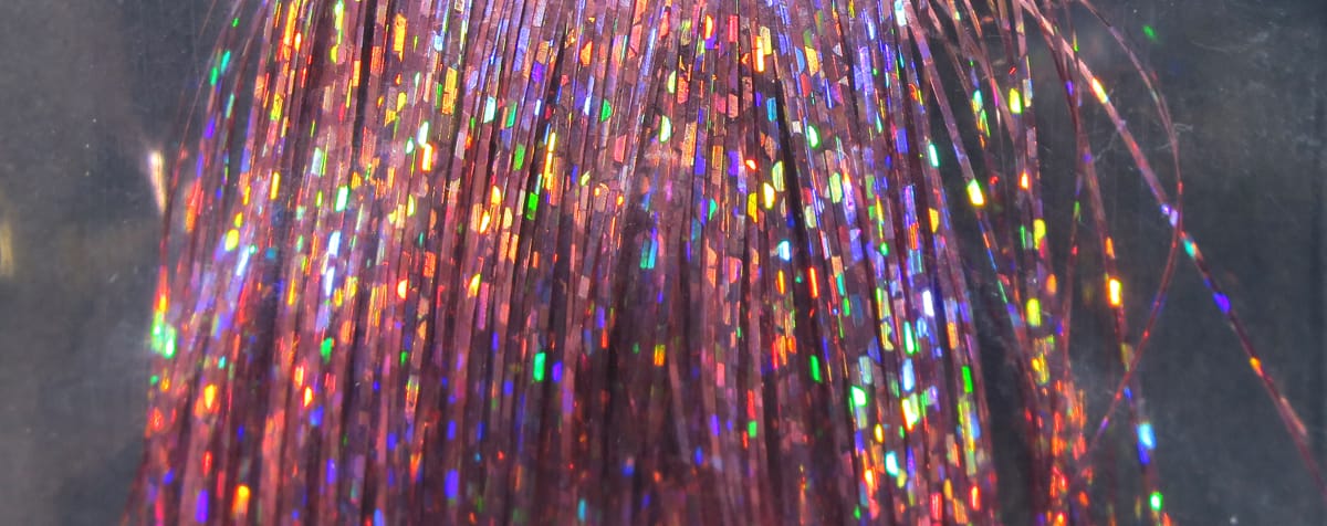 Hedron holographic Flashabou strands in pink-red with rainbow iridescent tinsel flashes, thin synthetic fly tying material
