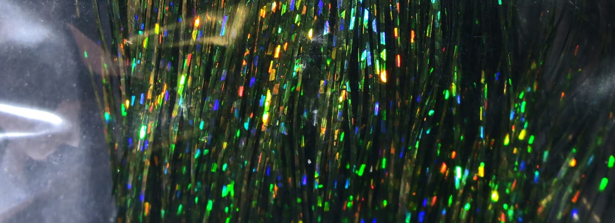 Hedron holographic Flashabou strands in dark green tinsel with multicolored reflective flakes, fly tying material.