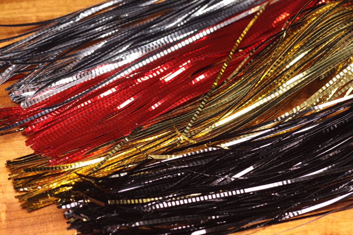 Hedron lateral scale fly tying tinsel strips in metallic red, gold, black and silver, ribbed reflective Mylar strands on wood
