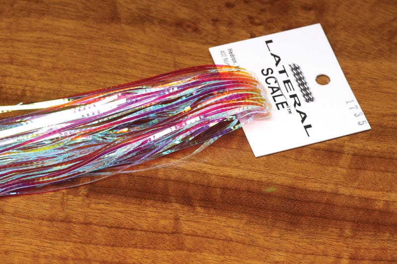 Hedron Lateral Scale fly tying iridescent holographic tinsel strips in pink, blue and silver on white tag over wooden surface