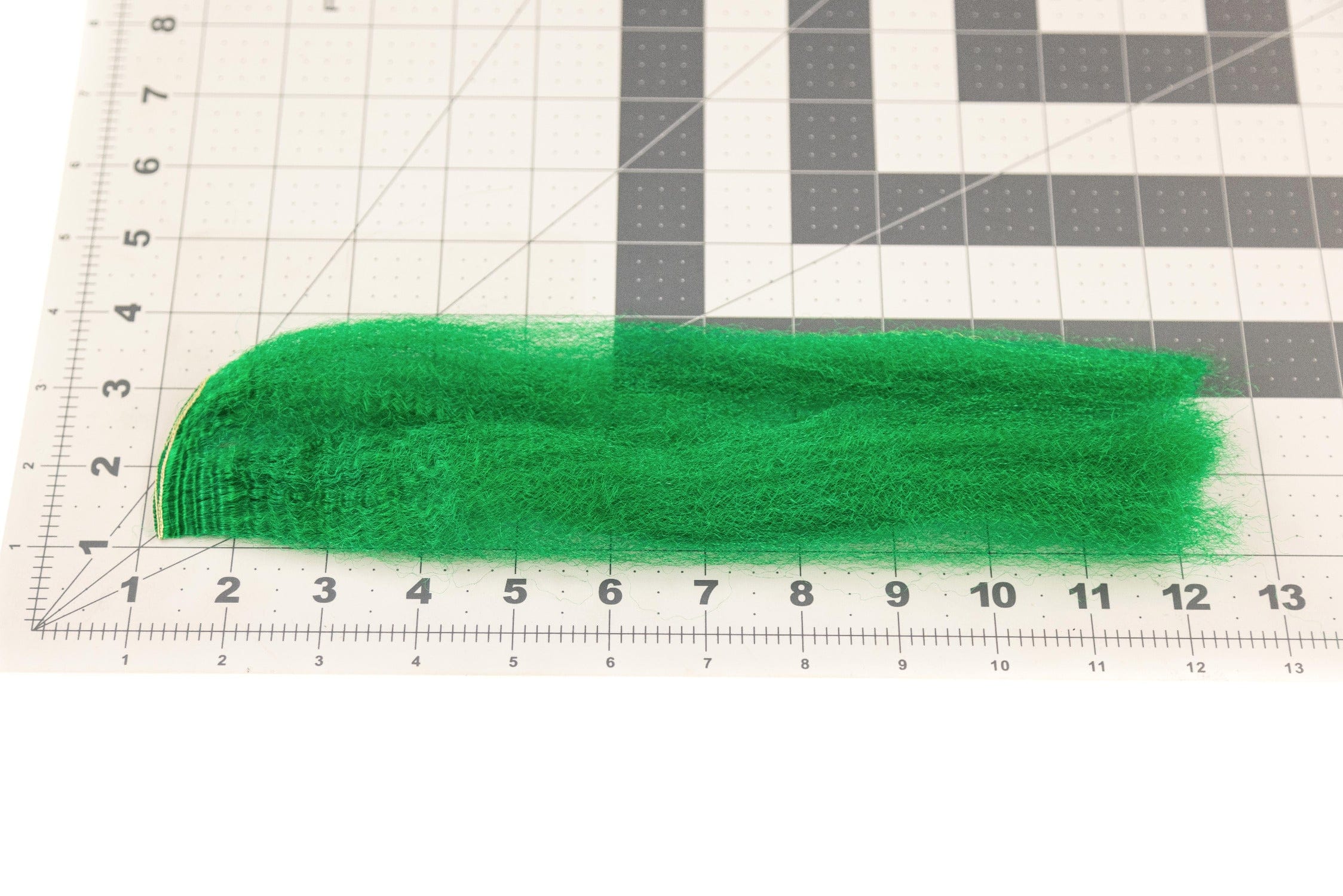 Bright emerald green strung fuzzy fiber for fly tying, long soft synthetic strands laid on gridded cutting mat