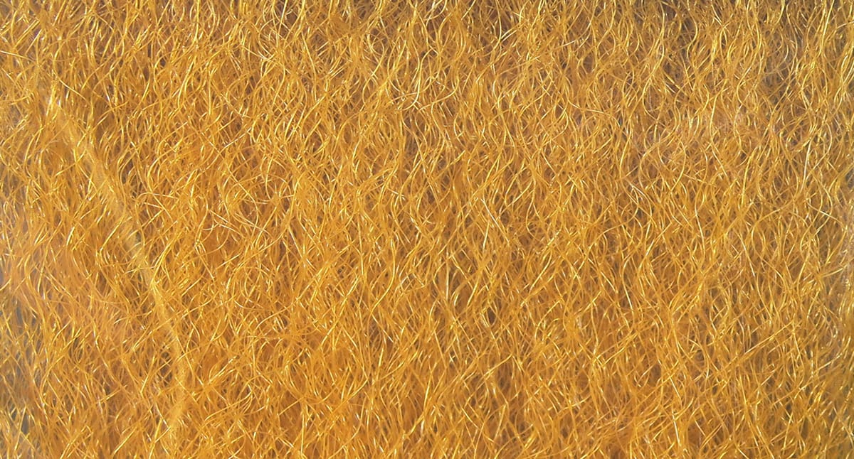 Golden-orange strung fuzzy synthetic fly tying fiber with fine curly shiny strands, dense textured material for tying flies