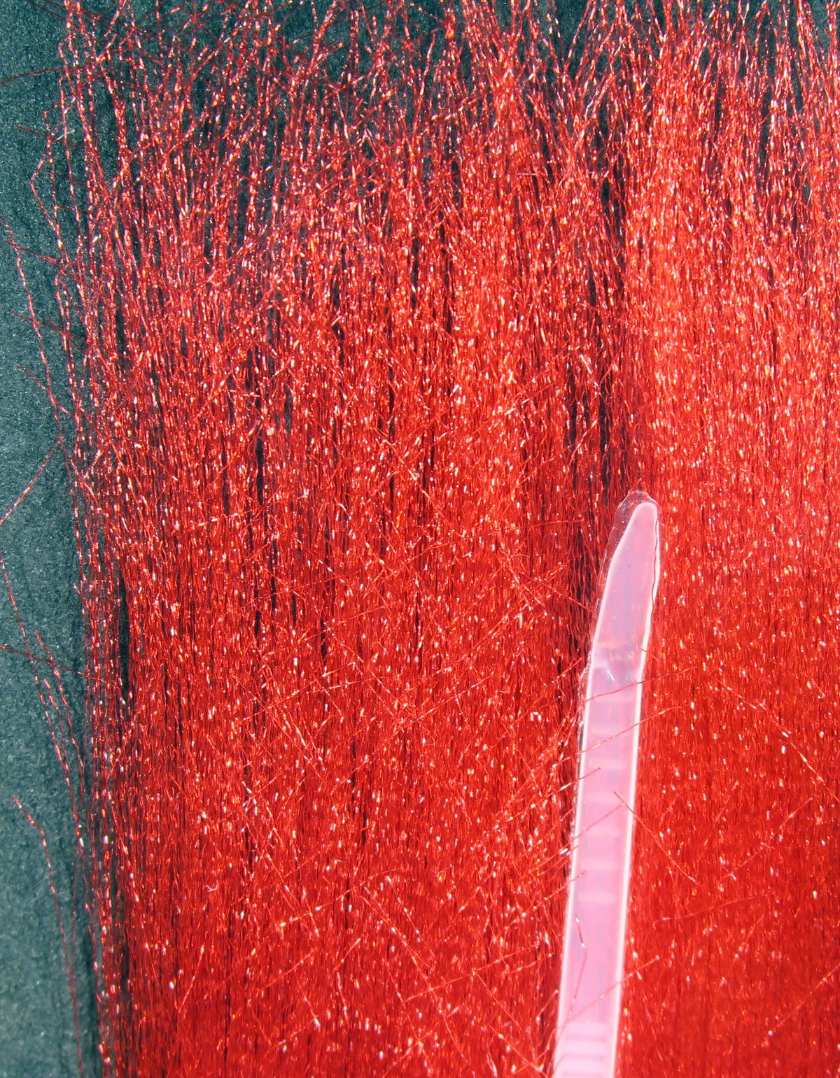 Bright red fluoro fibre strands with glittering metallic sheen, fine synthetic filaments for fly tying