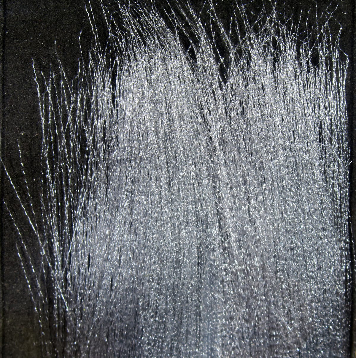 Silver translucent fluoro fibre strands with shimmery synthetic sparkle on black backing for fly tying