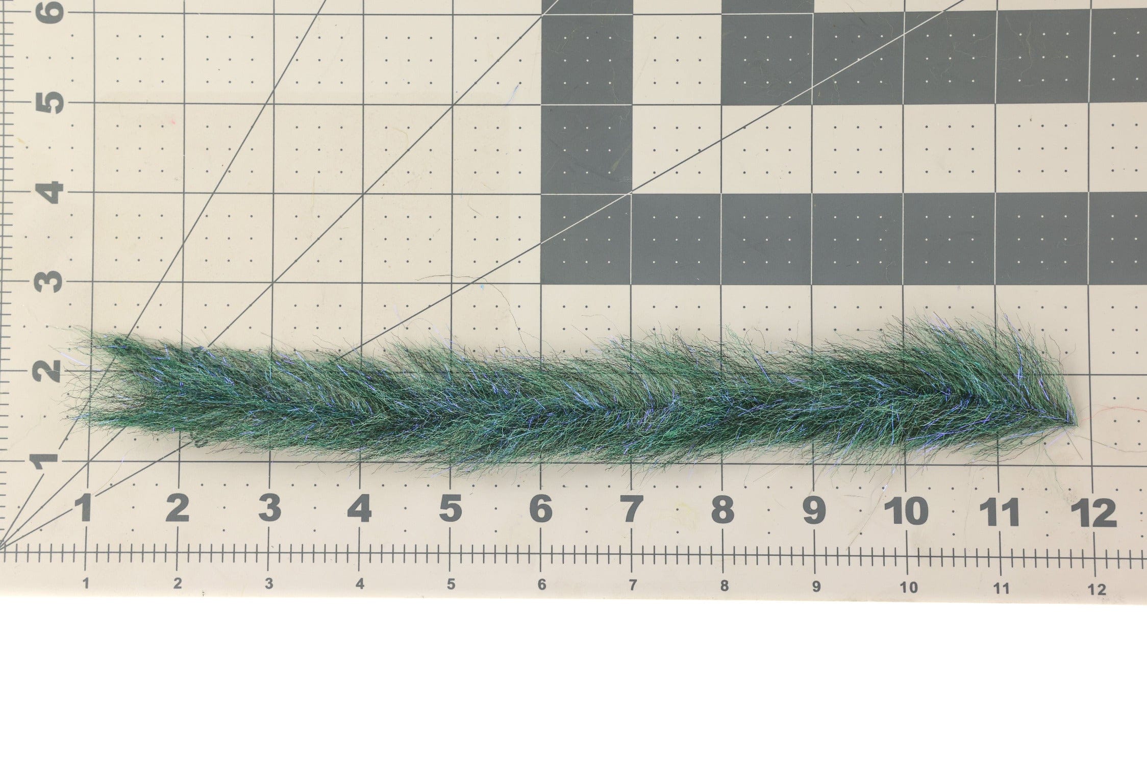 Green synthetic sculpting flash streamer brush with blue iridescent fibers laid on gridded ruler mat for fly tying