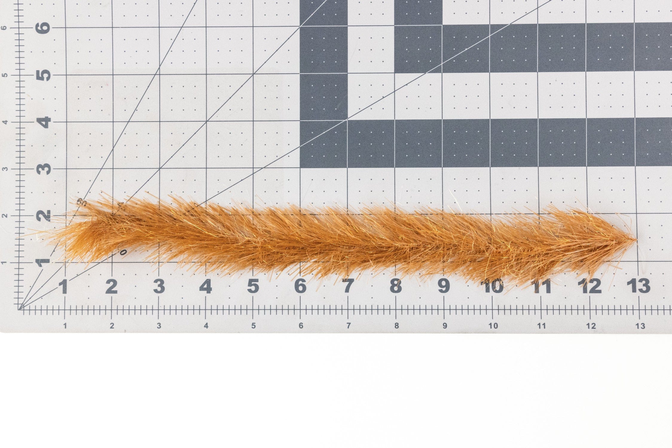 Translucy orange-gold synthetic fly brush strip with glittery fibers for fly tying laid on a grid measuring mat