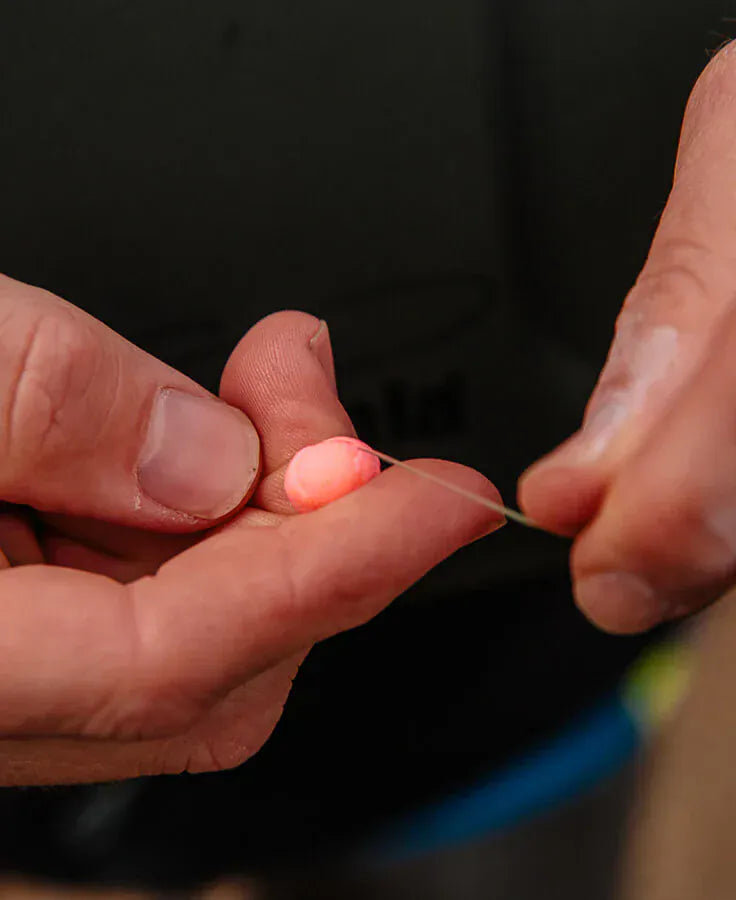 Hands threading neon pink soft foam Loon Biostrike fishing indicator bead onto clear fishing line