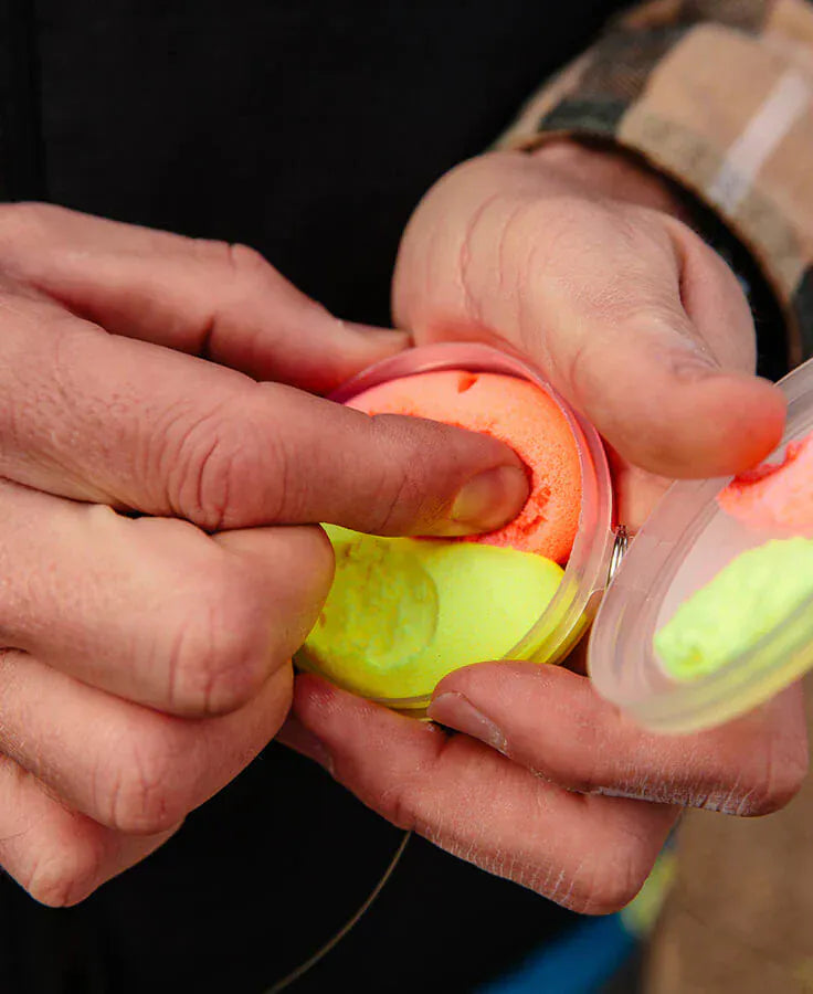 Hands pressing neon orange and chartreuse foam Loon Biostrike fishing indicator in clear plastic case