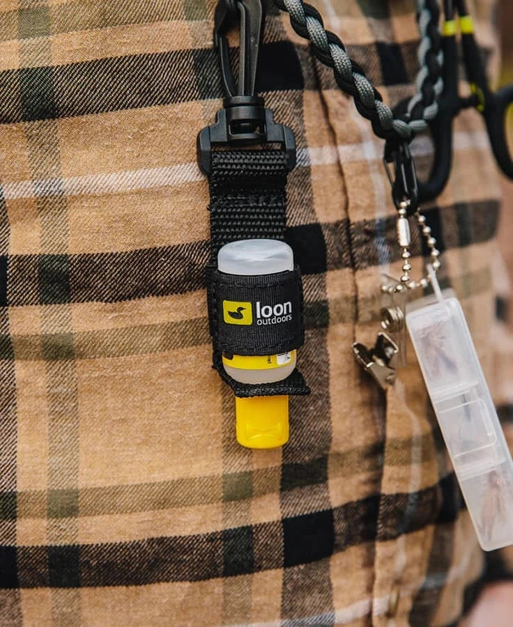 Black nylon Loon Caddy accessory clipped to brown plaid flannel, holding a yellow tube with Loon Outdoors logo and metal clip