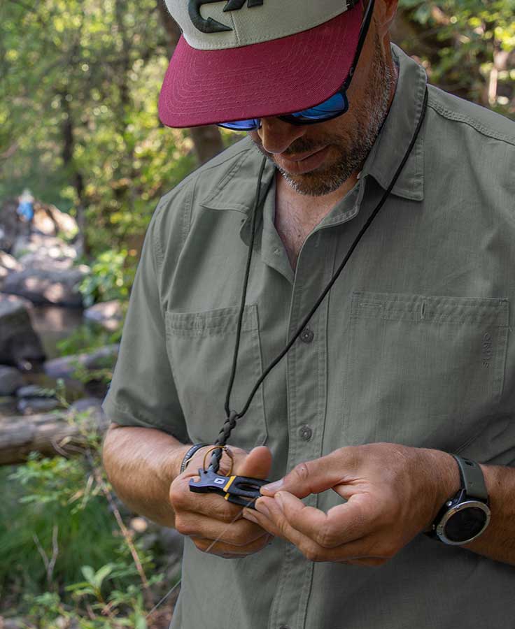 Man wearing Loon Spartan black braided cord lanyard with small black-and-yellow tool attached, outdoor fishing accessory