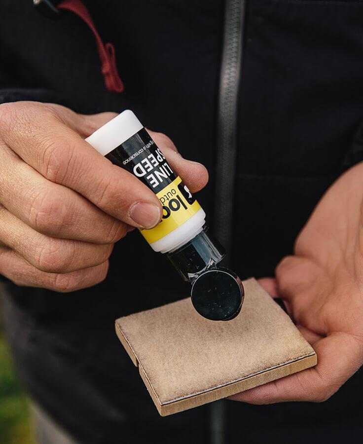 Hands applying Loon Line Speed clear dressing from white and yellow bottle onto tan suede pad for fly tying