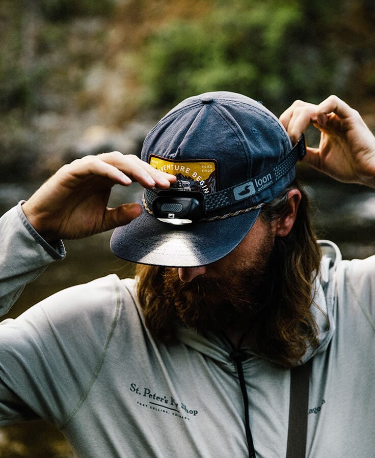 Loon Nocturnal black LED headlamp on gray cap with patterned adjustable strap, beam lighting brim, designed for fly tying