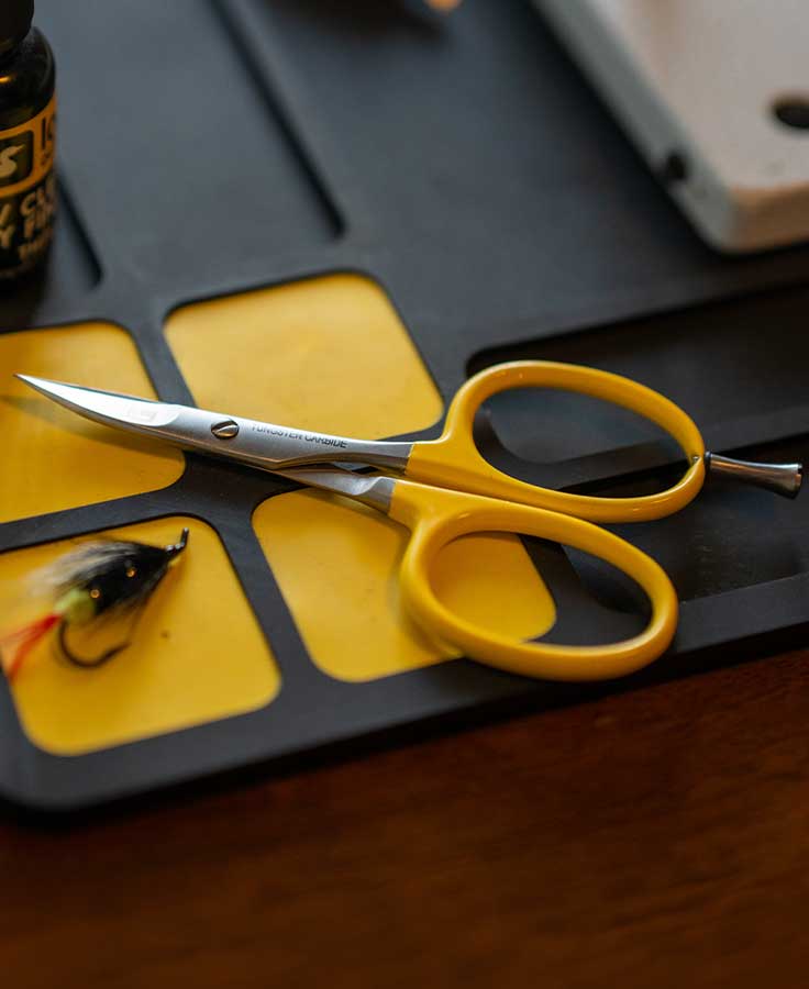 Yellow-handled Loon curved tungsten carbide fly tying scissors with silver curved blades on a black and yellow work mat