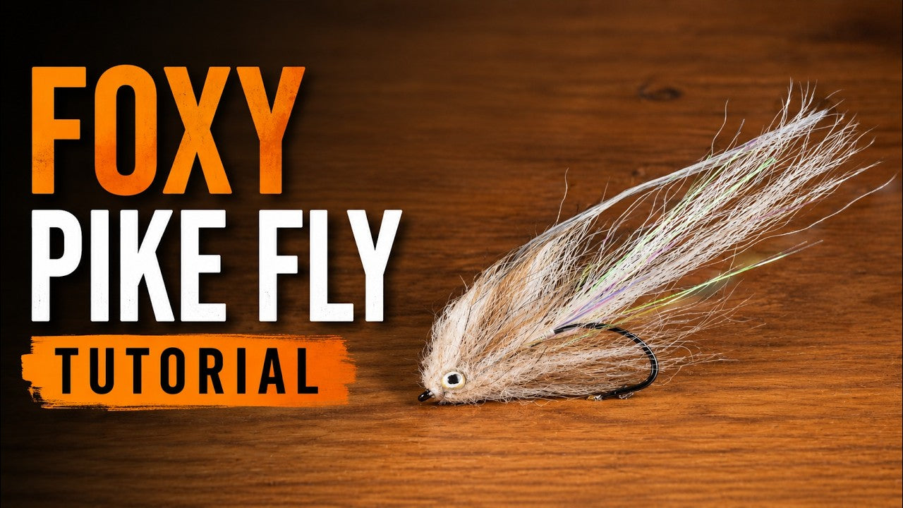 Tan fox fur baitfish fly with iridescent flash fibers and painted eye on a black hook, streamer fly style on wood
