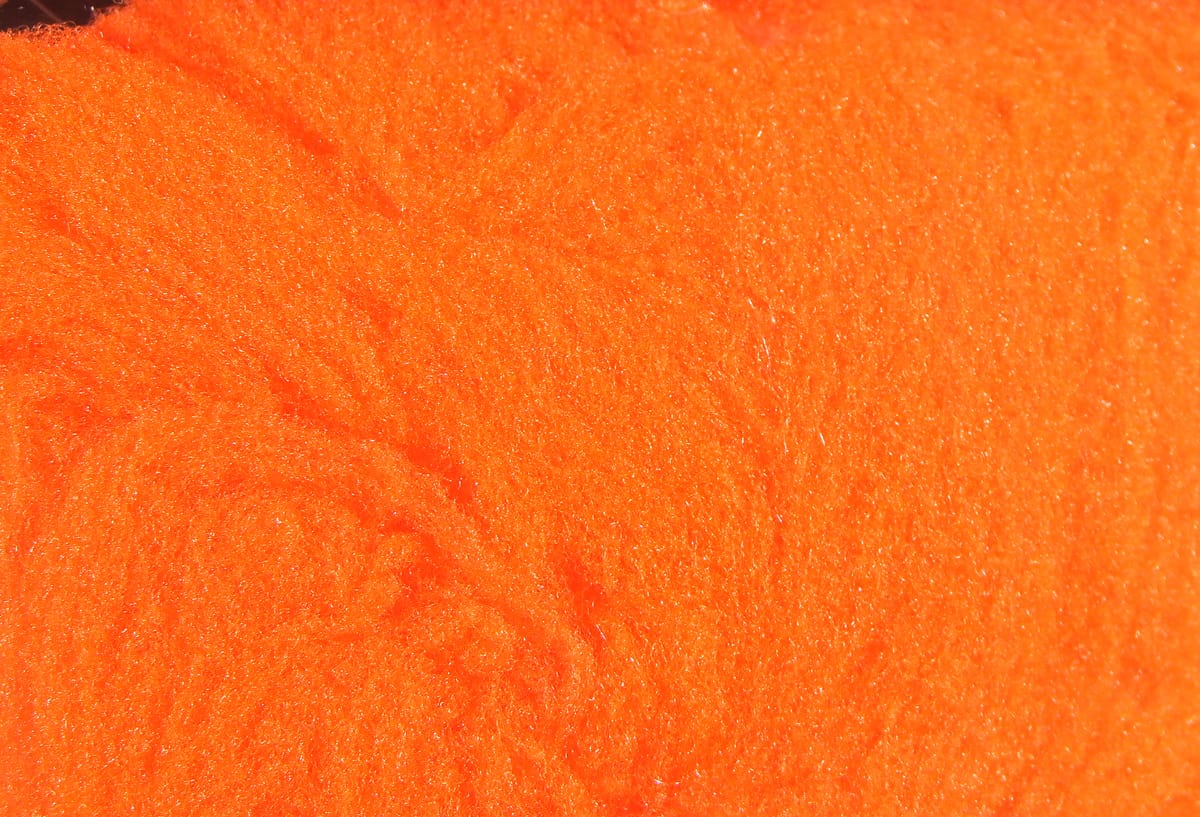 Bright neon orange fly tying yarn with fuzzy synthetic foam fibers and dense plush texture