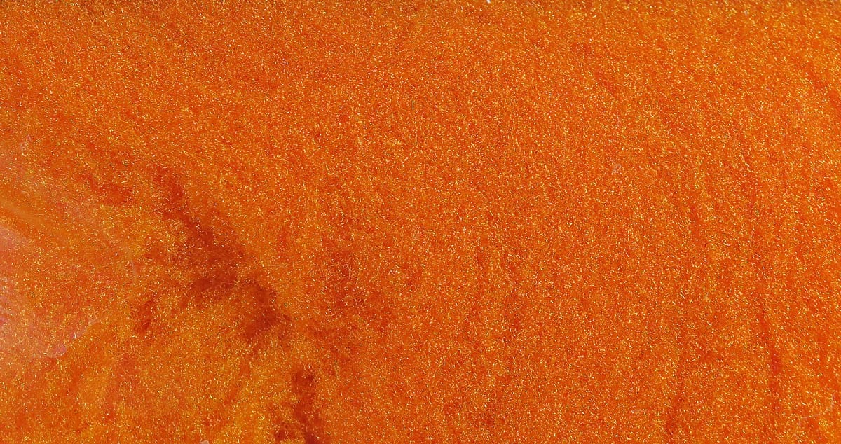 Bright orange McFlyFoam fly tying yarn close-up showing fine glittery foam fibers with gold shimmer