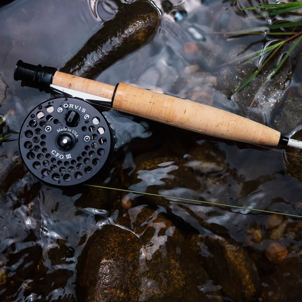 Orvis CFO III fly reel with cork handle rod displayed in shallow stream water among rocks and aquatic plants