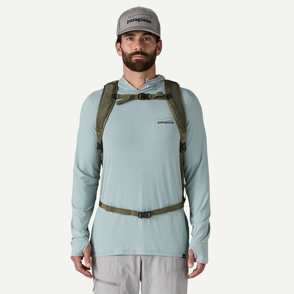 Male model wearing olive-green Patagonia Guidewater backpack harness with sternum and hip straps over light-blue pullover