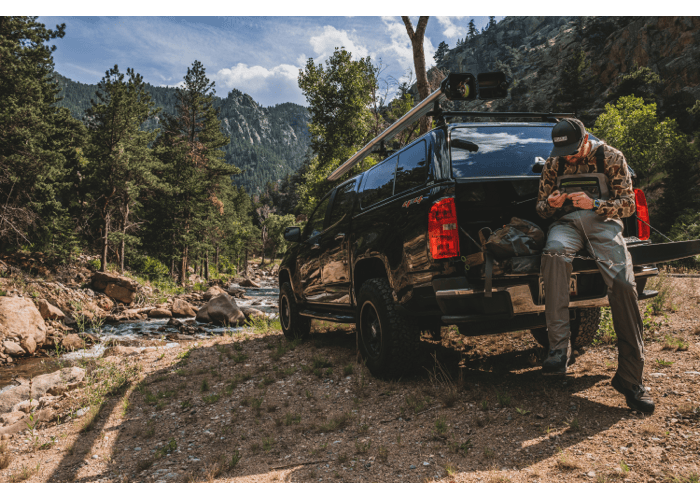 Riversmith Euro River Quiver fishing rod rack mounted on black van near mountain stream with forest backdrop