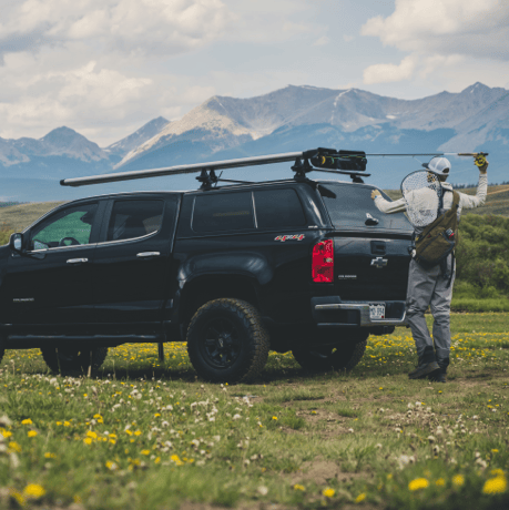 Black truck with Riversmith Euro River Quiver fishing rod rack mounted on roof, mountains in background