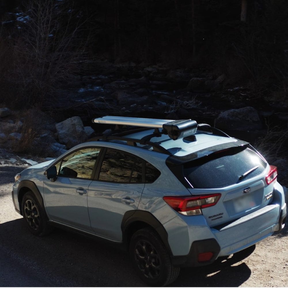 White Subaru with Riversmith ShortCut river quiver roof rack holding fishing rod carrier in forest setting