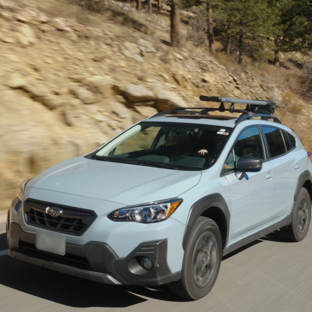 White Subaru Crosstrek SUV with black Riversmith ShortCut river quiver fishing rod rack mounted on roof rack during mountain