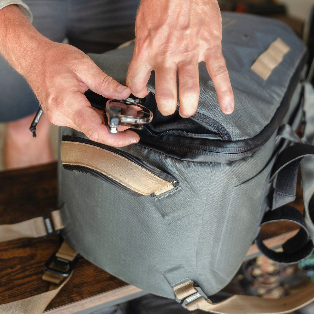 Man opening gray waterproof duffel bag with carabiner clip and multiple zippered pockets for gear storage